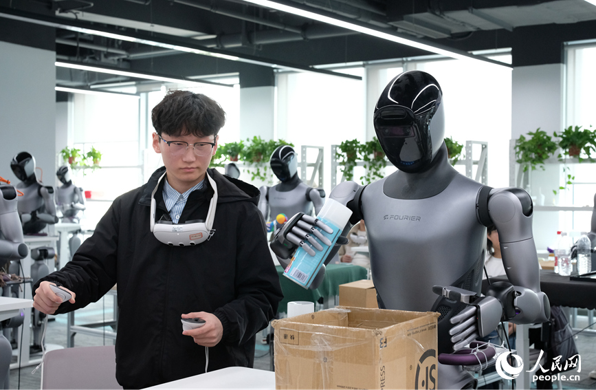 چین کے وسطی صوبے حہ نان کے شہر جینگ جو کے جونگ یوان سائنس اینڈ ٹیکنالوجی سٹی کے 4 ایس سٹور برائے مختلف النوع روبوٹس کے تربیتی مرکز میں تربیتی عملے کا رکن، روبوٹ کو چیز پکڑنے اور اسے رکھنے کی مشق کروا رہاہے ۔ (پیپلز ڈیلی آن لائن/چھانگ لی یوان)